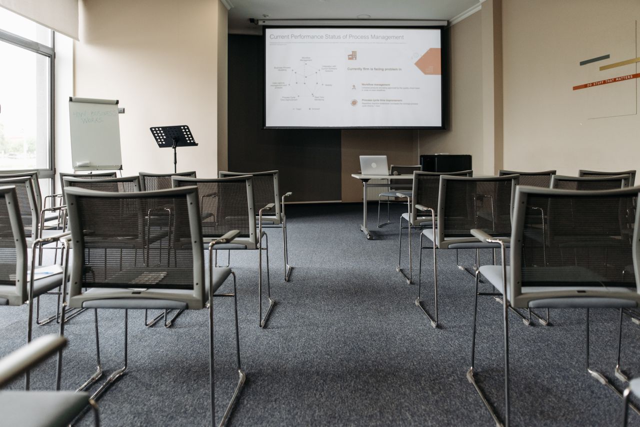 contact-hero An empty conference room with chairs, a projector screen, and presentation setup.